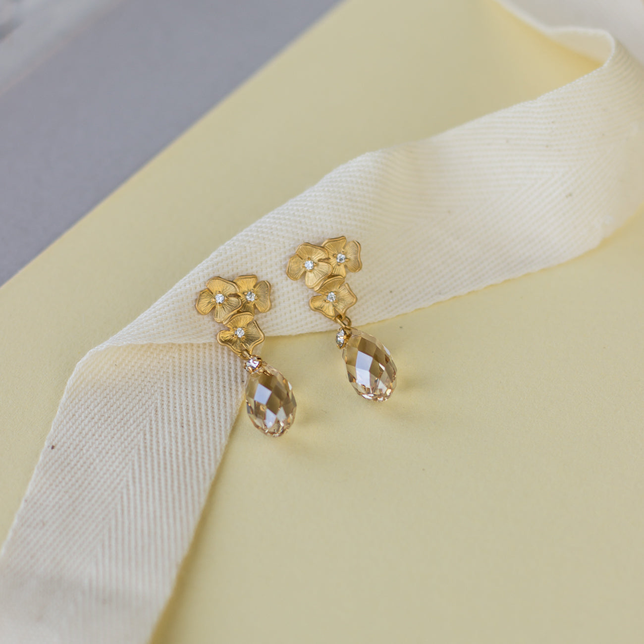 Discover these elegant crystal earrings featuring delicate floral studs and drop-shaped Swarovski golden shadow crystals, perfect for any occasion.